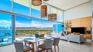 Un salon moderne doté d’une grande fenêtre, un coin repas avec une table et des chaises, un canapé et un téléviseur à écran plat.
