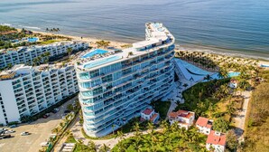 Un hôtel à plusieurs étages doté d’une piscine sur le toit, situé près d’une plage bordée de palmiers.
