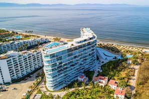 A multi-story hotel with a pool on the rooftop, located near a beach with palm trees. - Oceanfront luxury with amazing view, 4 pools, private beach, on-site spa, dining (Bucerias)