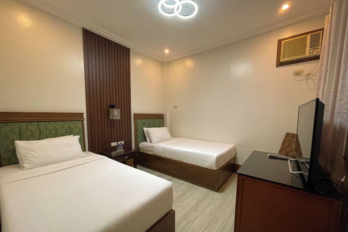 A hotel room with two beds, a desk, a television, and a mirror.