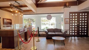 Un espace d’accueil doté d’un plafond en bois, d’un comptoir de réception, d’une barrière en corde rouge, d’un canapé en cuir marron et d’une petite table ronde.