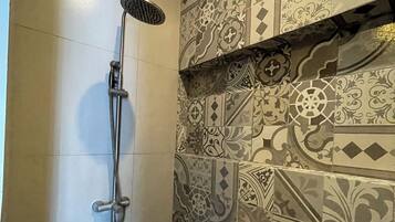 A shower with a handheld showerhead, a wall with patterned tiles, and a plain tiled floor.