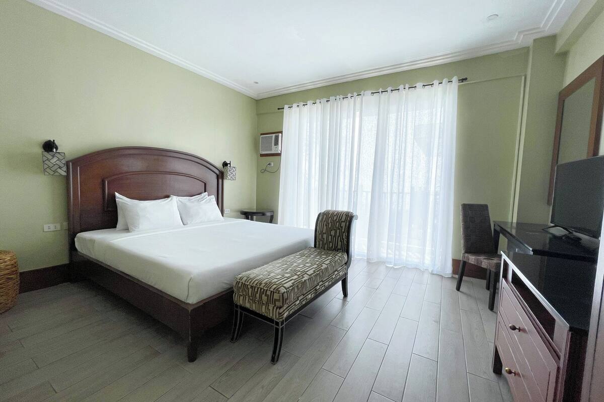 A hotel room with a bed, a bench, a chair, a TV, and a desk.
