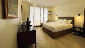 Une chambre d’hôtel avec un lit, des tables de chevet, un bureau, une chaise, une télévision et un tableau au mur.