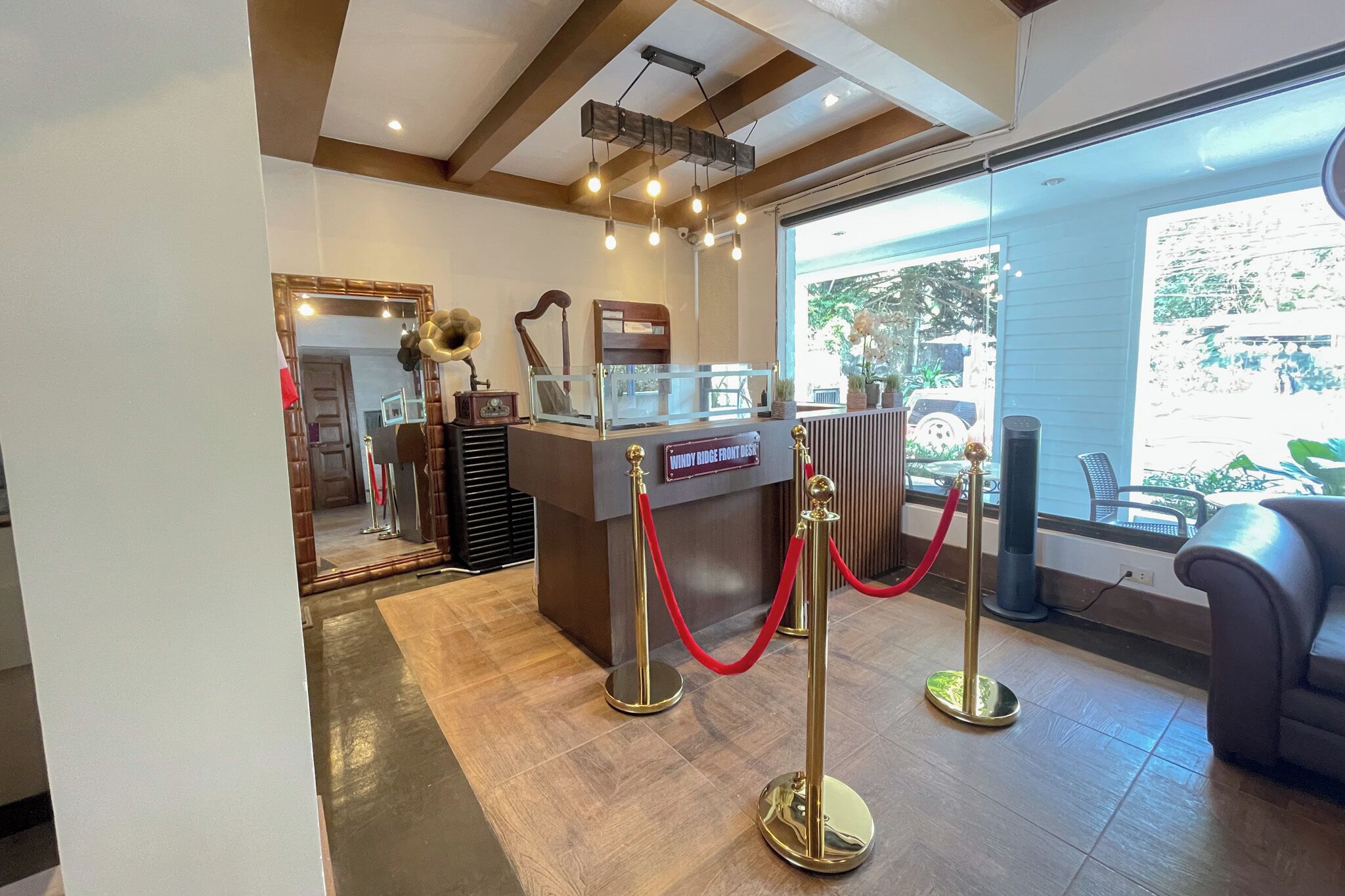 A reception desk with a red rope barrier, a large mirror, and a view of the outdoors through a glass door.