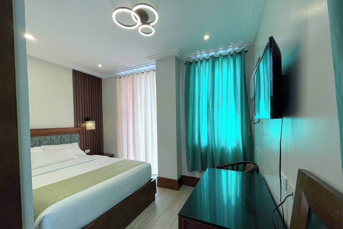 A hotel room with a bed, a desk, a television, and a window with curtains.