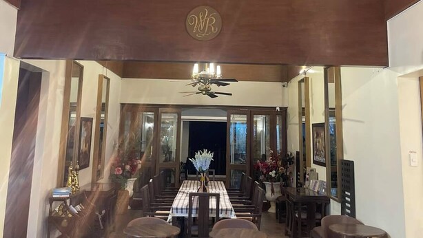 Une salle à manger spacieuse, agrémentée d’un grand lustre, de poutres en bois au plafond et d’une table centrale entourée de chaises.