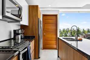 A modern kitchen with a built-in oven, microwave, and coffee maker, leading to a wooden door. - Ocean-view Bucerías condo near beach, dining & shops (Bucerias)