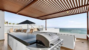 Um bar no terraço com churrasqueira, área de estar e vista para o mar.