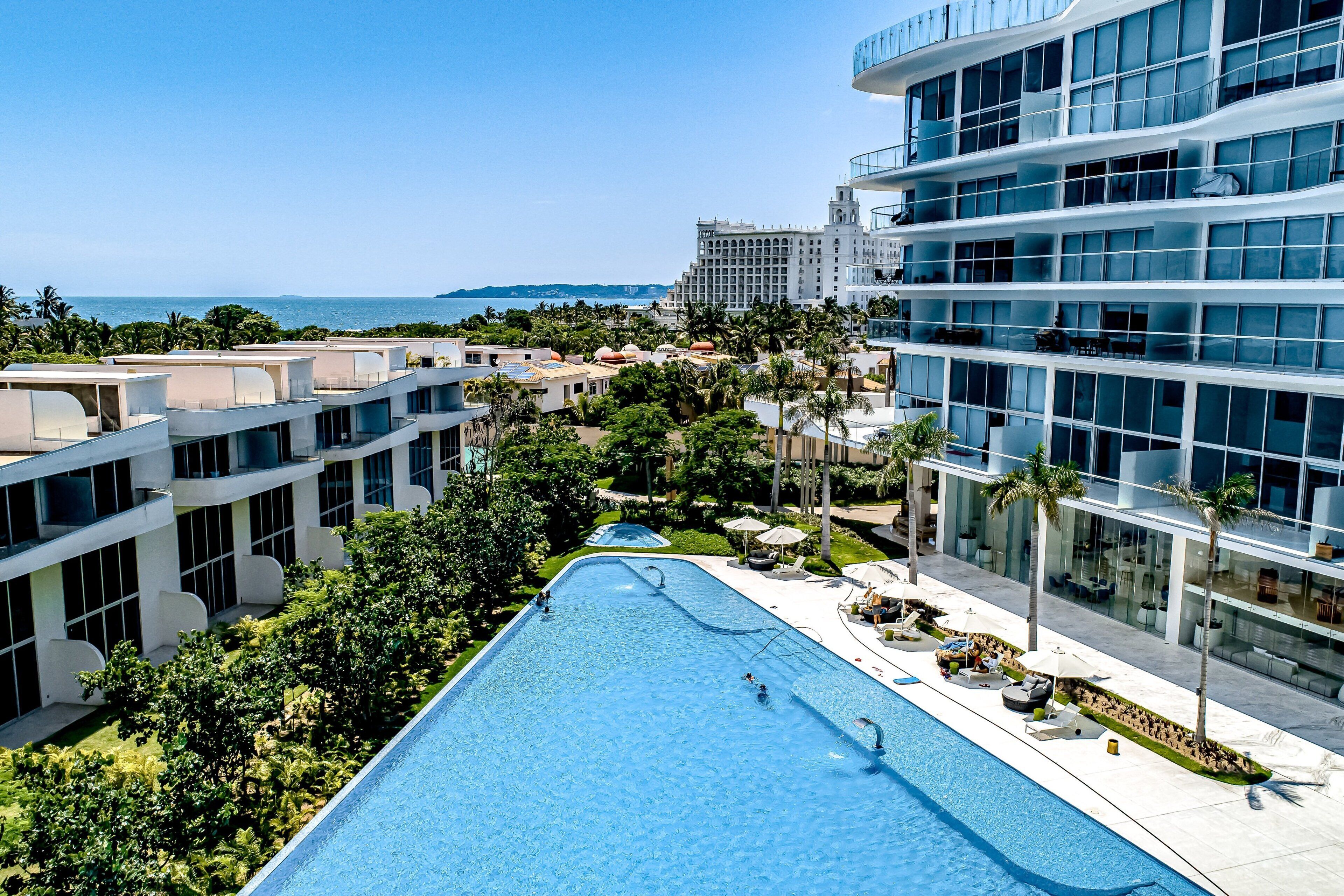 Un hôtel moderne doté d’une grande piscine, de palmiers et offrant une vue sur l’océan.