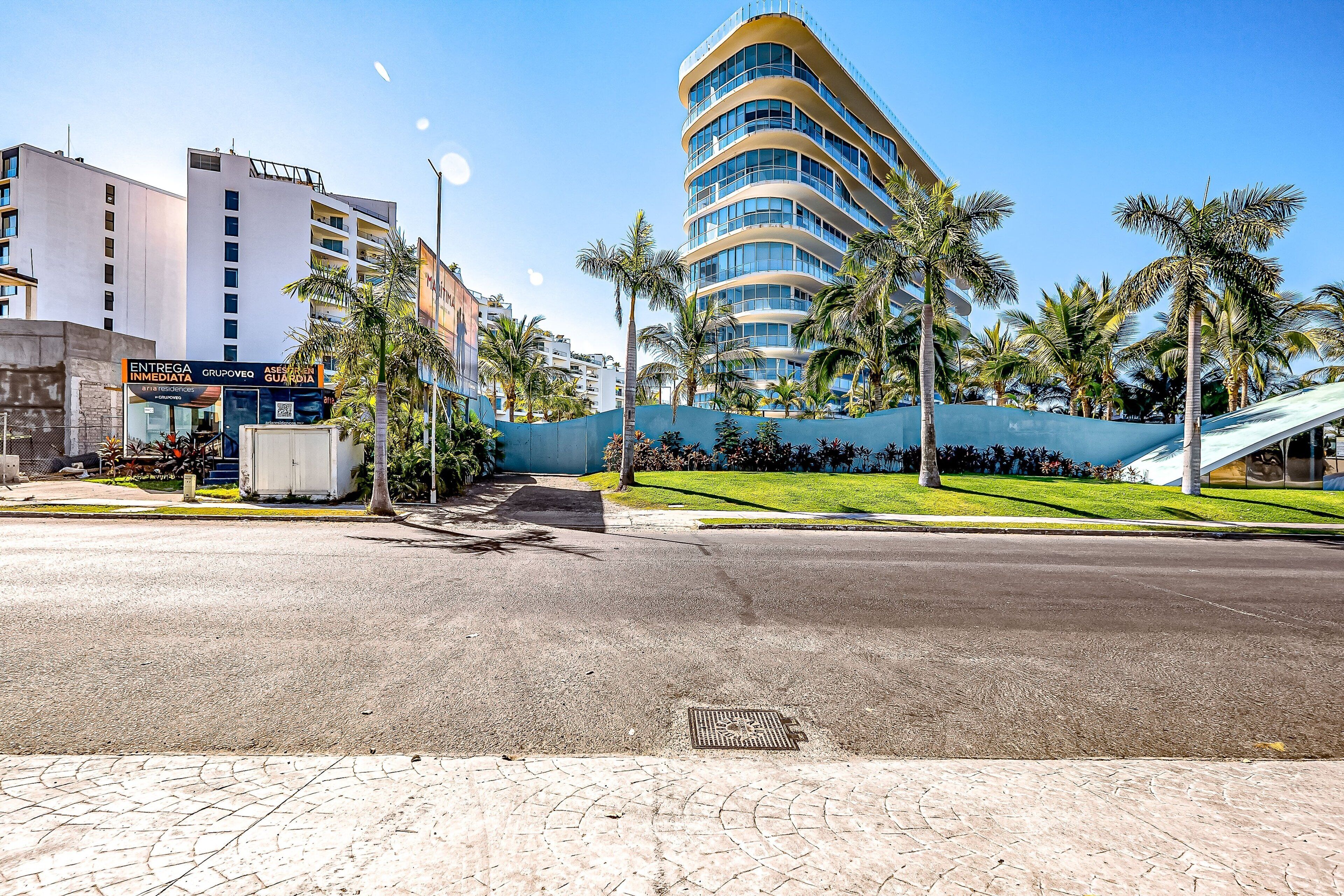 A modern building with a curved facade, palm trees, and a paved street.