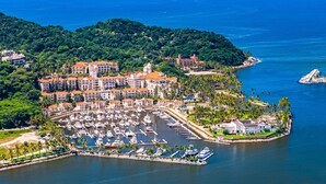 A marina with boats, a hotel with red roofs, and a forested hill.