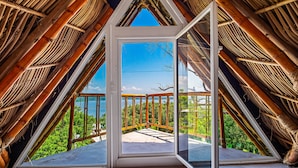 A room with a large glass door leading to an outdoor balcony with a view of greenery and a clear sky.
