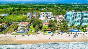 A coastal hotel with multiple buildings, a beach, and palm trees. - Luxury Beachfront Condo | Resort Pool, Ocean Views, Walk to Beach (Nuevo Vallarta)