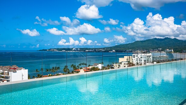 Een resort met een zwembad, gebouwen en uitzicht op de oceaan en bergen.