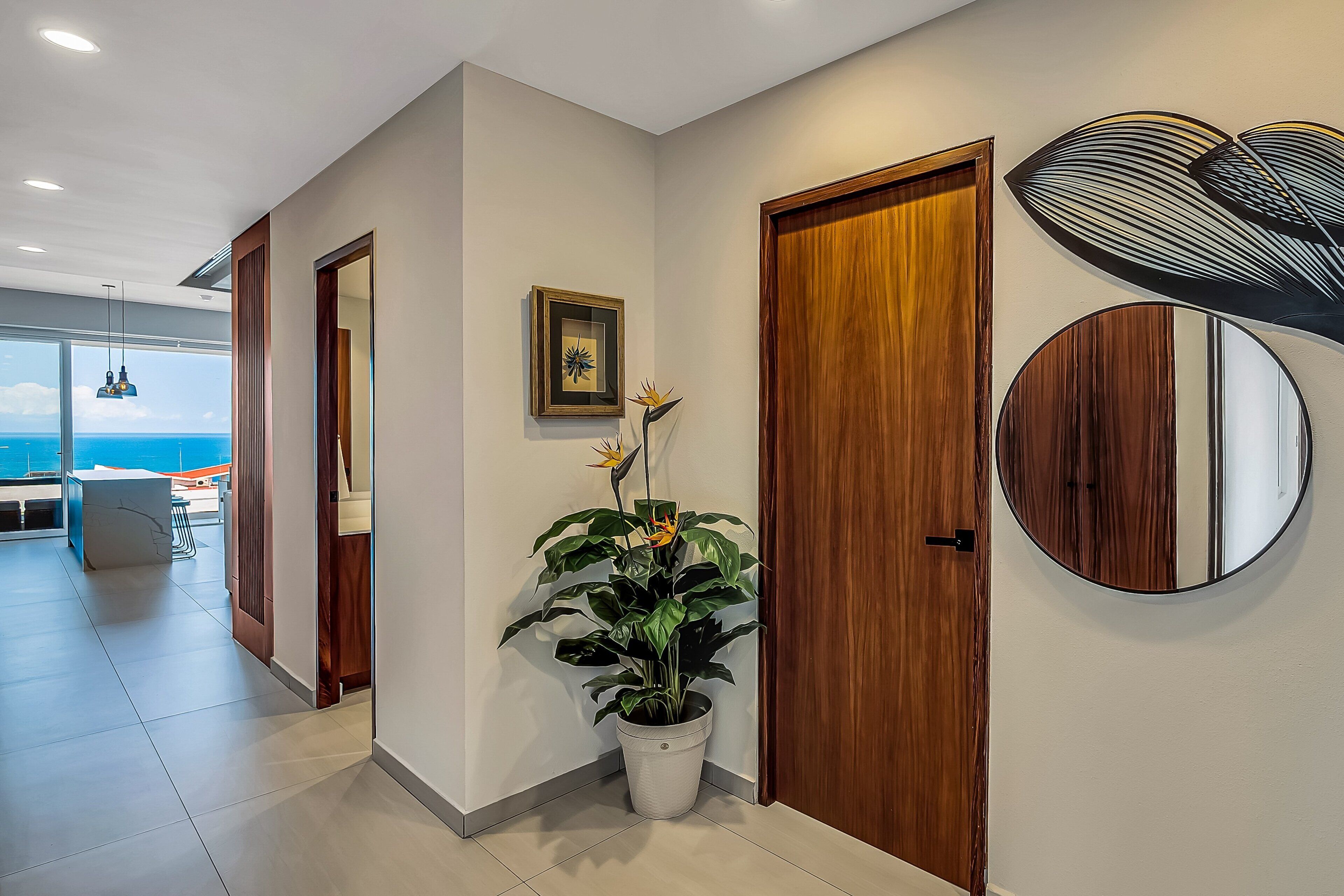 A modern hallway with a potted plant, wooden doors, a framed picture, and a round mirror on the wall.