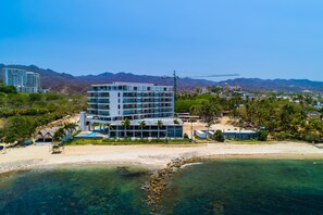 A modern hotel with multiple floors, a beach view, and a crane in the background. - Seabreeze Haven | Oceanview studio, pool & gym (Cruz de Huanacaxtle)
