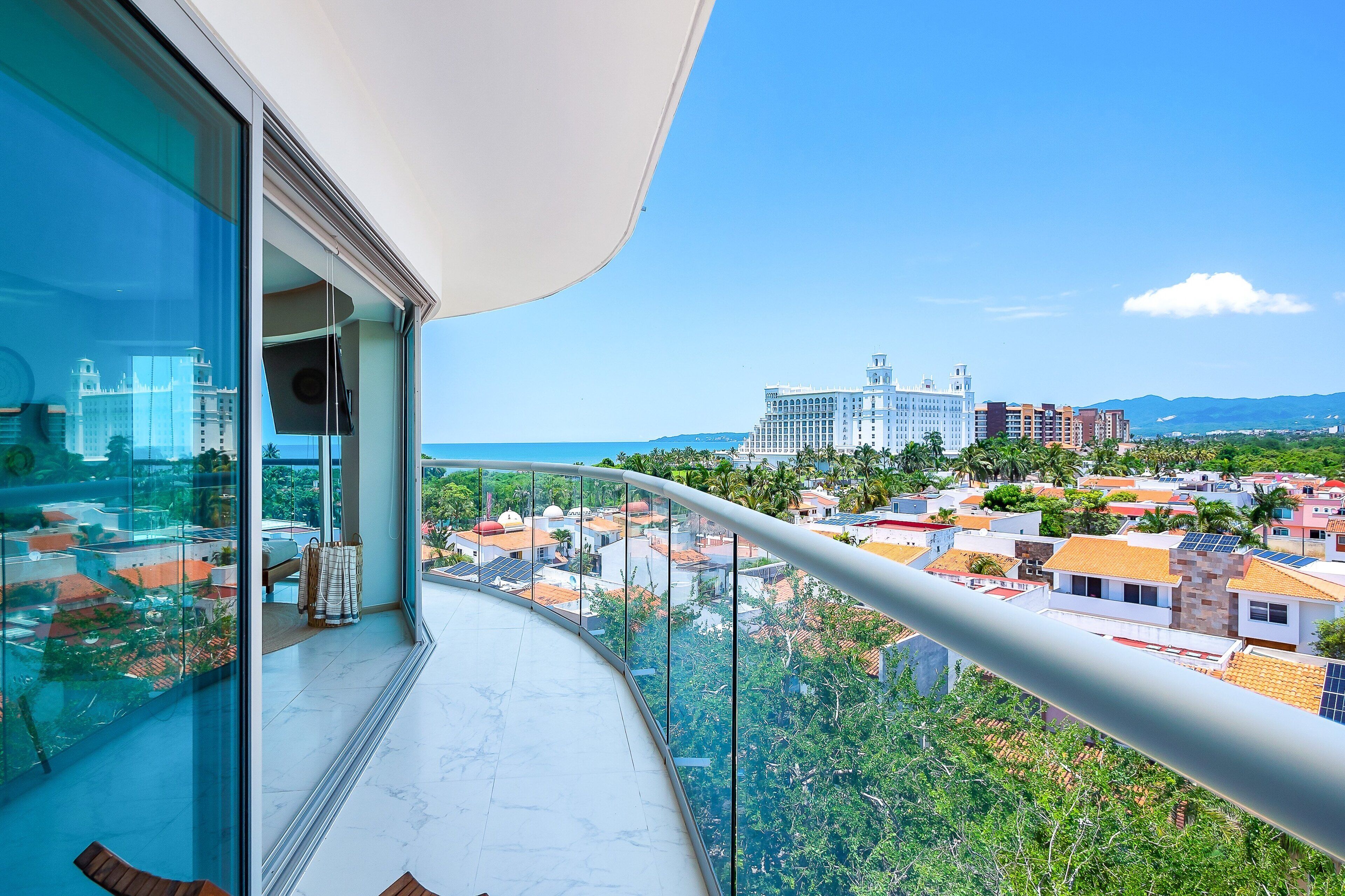 A balcony with a glass railing overlooking a residential area and a distant building.