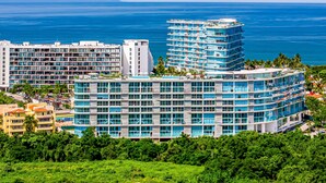 A multi-story hotel with a curved facade, large windows, and a view of the ocean. - Ocean-view condo with balcony, central AC, pool, gym, cinema, & bar (Nuevo Vallarta)
