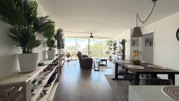 Uma sala de estar ampla com varanda, plantas em vasos, mesa de jantar e ventilador de teto.