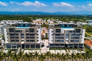 A modern hotel with a rooftop pool, multiple floors, and a view of surrounding greenery and distant mountains. - Punto Novo 504 | 1BR Nuevo Vallarta, Near Beach, Pool (Nuevo Vallarta)