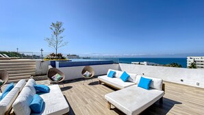 Een terras op het dak met een zwembad, witte banken met blauwe kussens en uitzicht op zee.