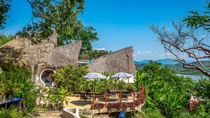 A thatched-roof structure with a circular window, outdoor seating with umbrellas, and lush greenery. - Coastal Couples Retreat | Plunge Pool + Hammocks (La Culebra)