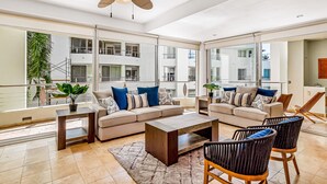 A spacious living area with a sofa set, coffee table, and chairs, large windows, and a ceiling fan. - Luxury Beach Condo | Community Pool, Ocean Views, Walk to Beach (Nuevo Vallarta)