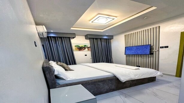 A modern hotel room with a bed, a TV mounted on the wall, and a small table. - Supreme Apartments (Ibadan)