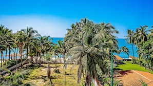 A tropical resort with palm trees, a pool, and a view of the ocean. - Beachfront Resort Condo w/ Pool, Rooftop Lounge & Tropical Ocean Views (Nuevo Vallarta)