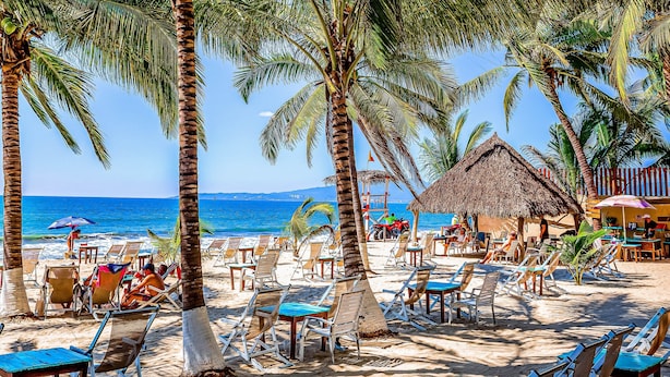 A beach with palm trees, lounge chairs, and a thatched-roof hut. - Beachfront Resort Condo w/ Pool, Rooftop Lounge & Tropical Ocean Views (Nuevo Vallarta)