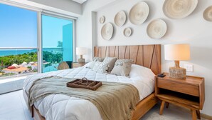 Ein modernes Schlafzimmer mit einem großen Bett, einem Nachttisch aus Holz und Blick auf einen Pool und Gebäude.