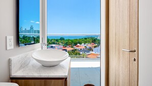Ein Badezimmer mit einem großen Spiegel, einem weißen Waschbecken und Blick auf eine Stadtlandschaft vom Balkon aus.