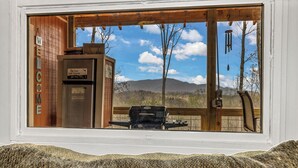 A view through a window of a wooden deck with a grill, a sign for Old Fort Golf Course, and a wooden pergola.