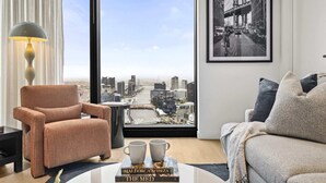 Un salon moderne avec une grande fenêtre, un canapé, un fauteuil, une lampe et un tableau encadré au mur.