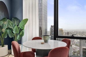 A modern room with a round table, red chairs, a large potted plant, and a view of a cityscape through a large window. - 1BR Apt |Pool, Gym Near Casino & Southbank Dinning (Southbank)