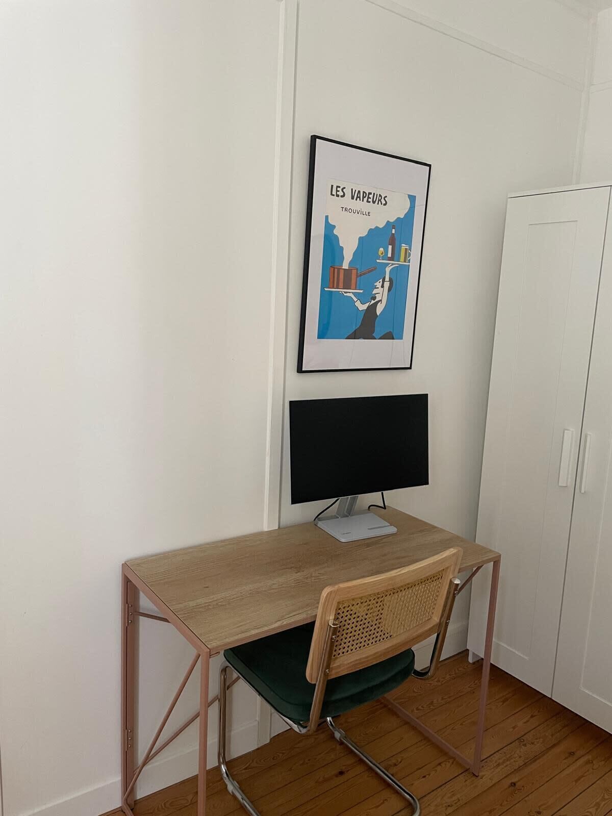 A small office space with a desk, chair, and a framed picture on the wall.