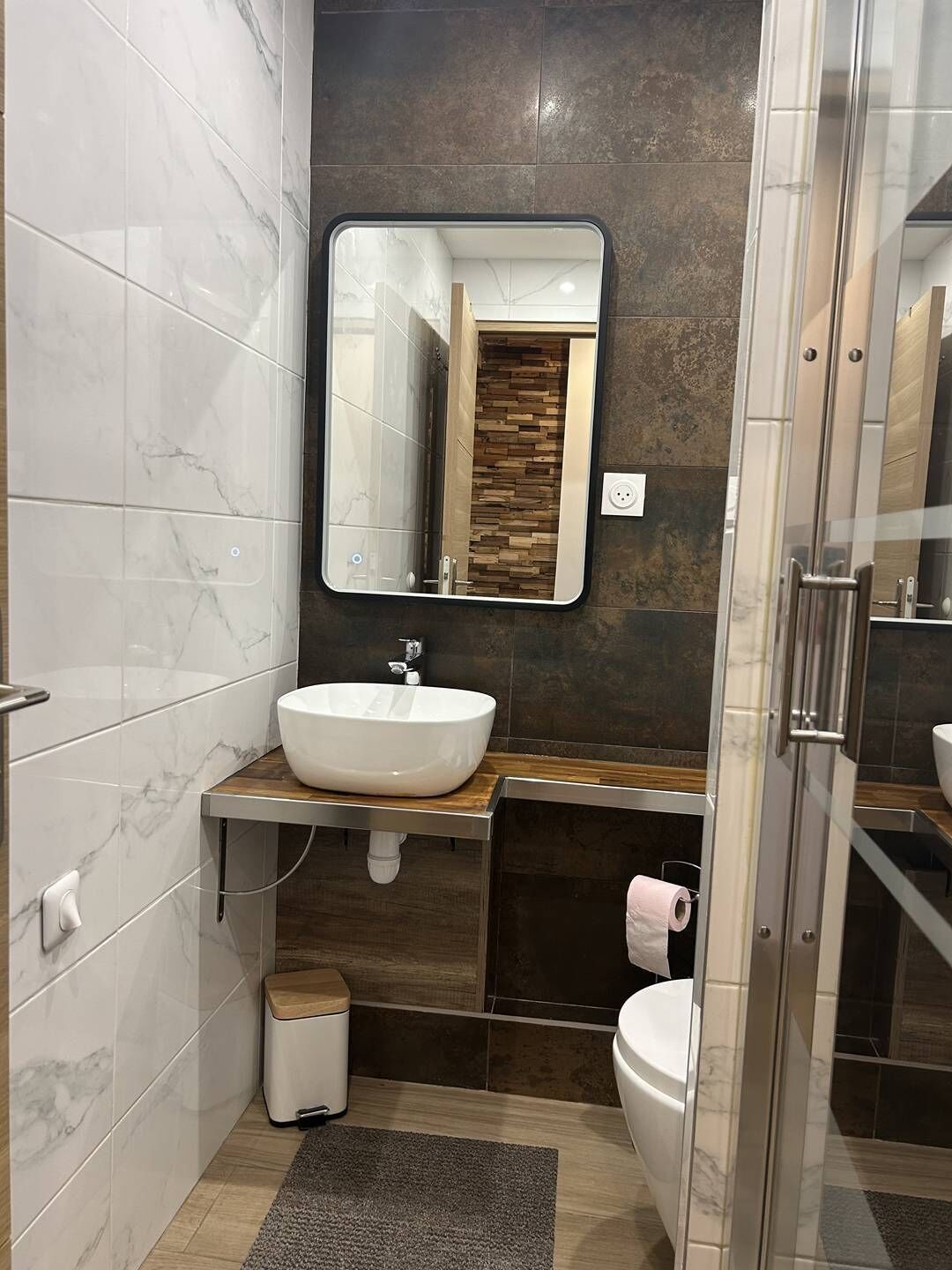 Ein modernes Badezimmer mit Marmorwaschtisch, einem großen Spiegel, einer Toilette und einer Duschkabine.