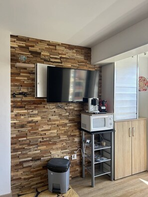 Una kitchenette con microondas integrado, un refrigerador pequeño y un televisor montado en una pared de madera.