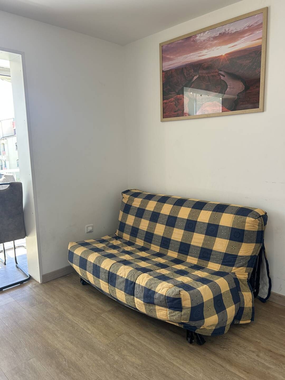 Una habitación con un sofá a cuadros, un cuadro en la pared y una puerta que da a un espacio exterior.