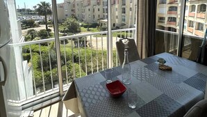 A balcony with a table, chairs, and a view of buildings and greenery. - Lovely 2-room with cabin apartment near the port and shops in Cap d'Agde (LE CAP D AGDE)