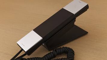 A black telephone with a coiled cord on a wooden surface.