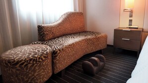 Une chambre d’hôtel avec un canapé, une petite table de chevet, une lampe et un lit.