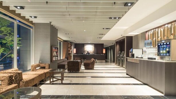 Un hall d’hôtel comprenant un comptoir d’accueil, un espace salon et une grande fenêtre donnant sur la rue.