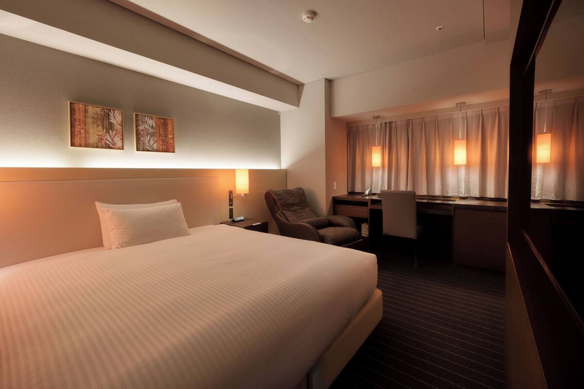 Habitación de hotel con una cama grande, un escritorio, una silla y dos lámparas fijadas a la pared.