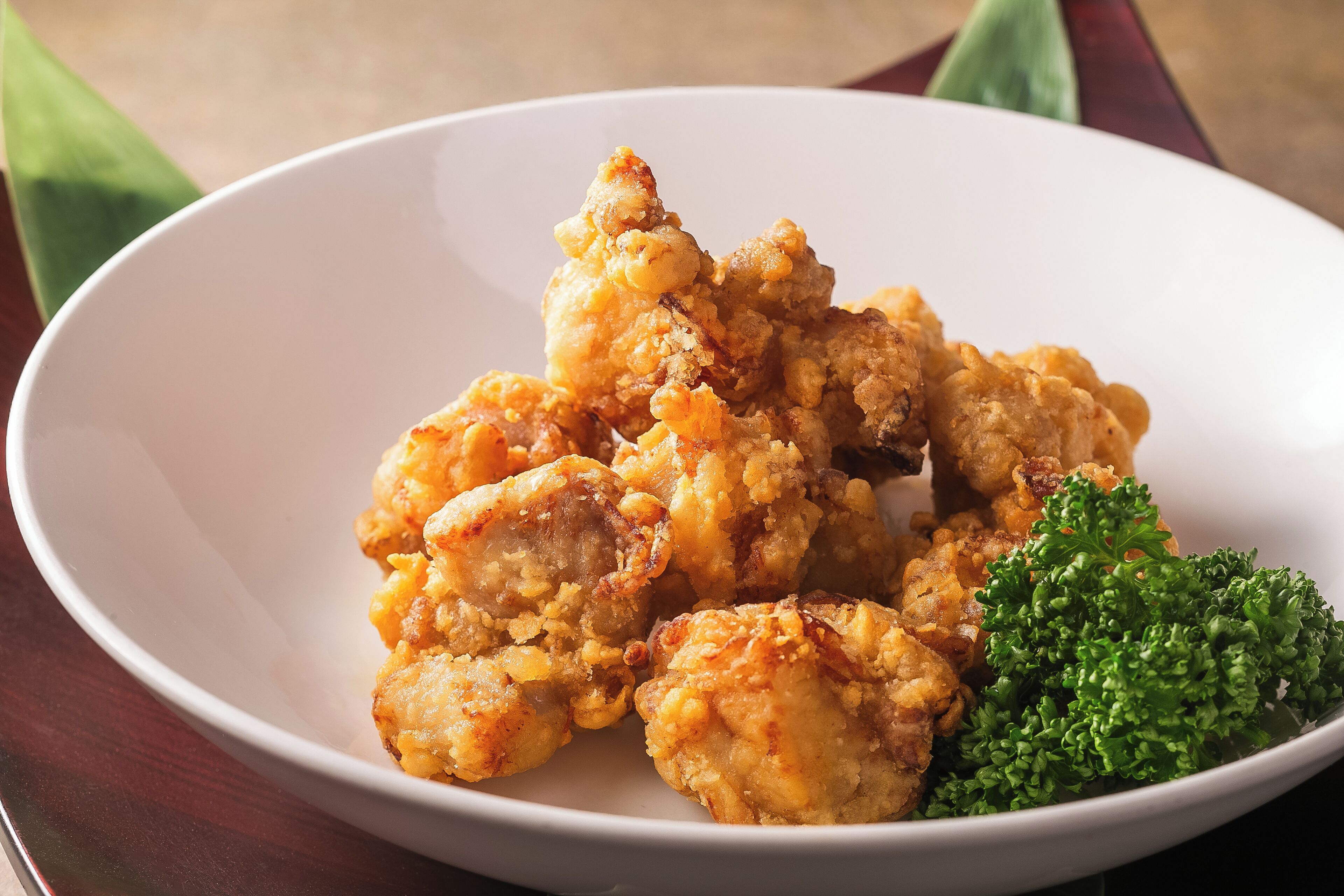 A white bowl with fried food and a green garnish on a table.