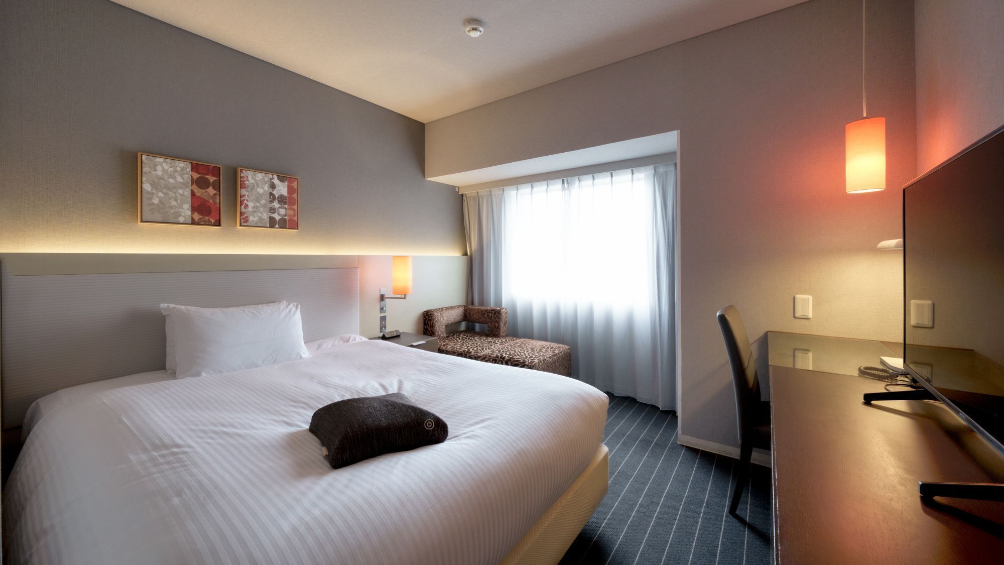 Habitación de hotel con una cama grande, un escritorio, una silla, una lámpara y una ventana con cortinas.