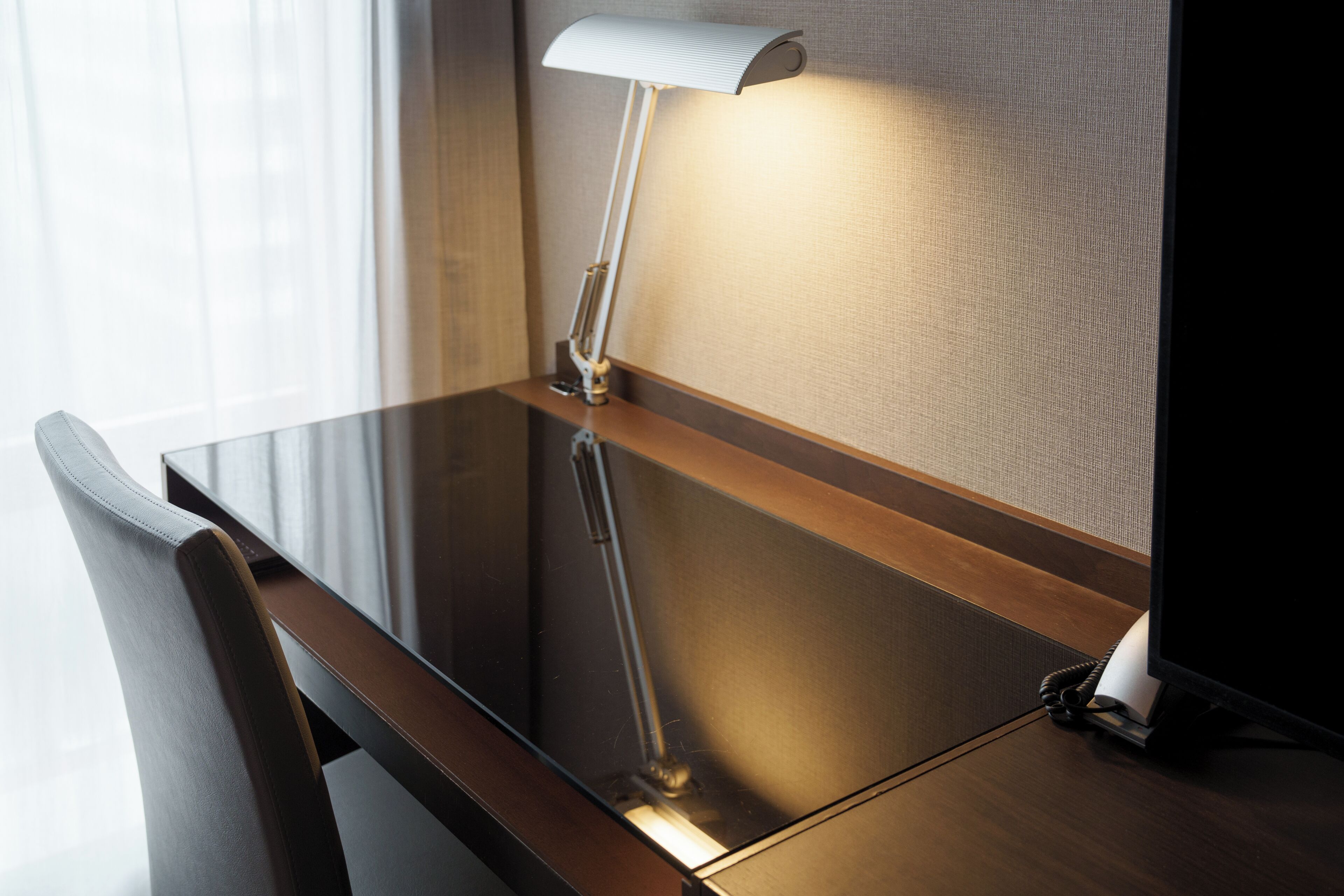 A modern desk with a lamp, a chair, and a telephone.