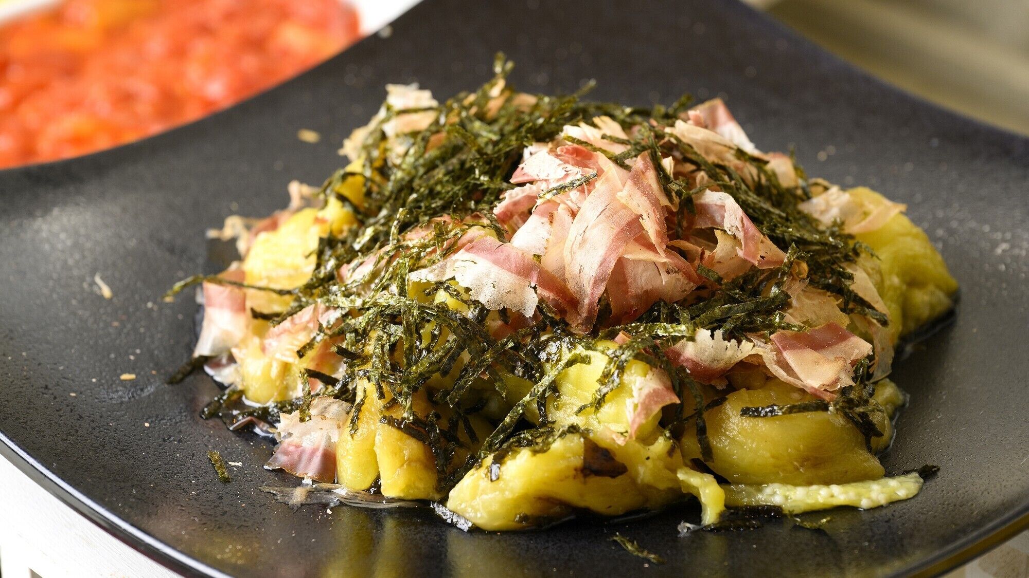 A dish with potatoes, bacon, and seaweed on a black plate.