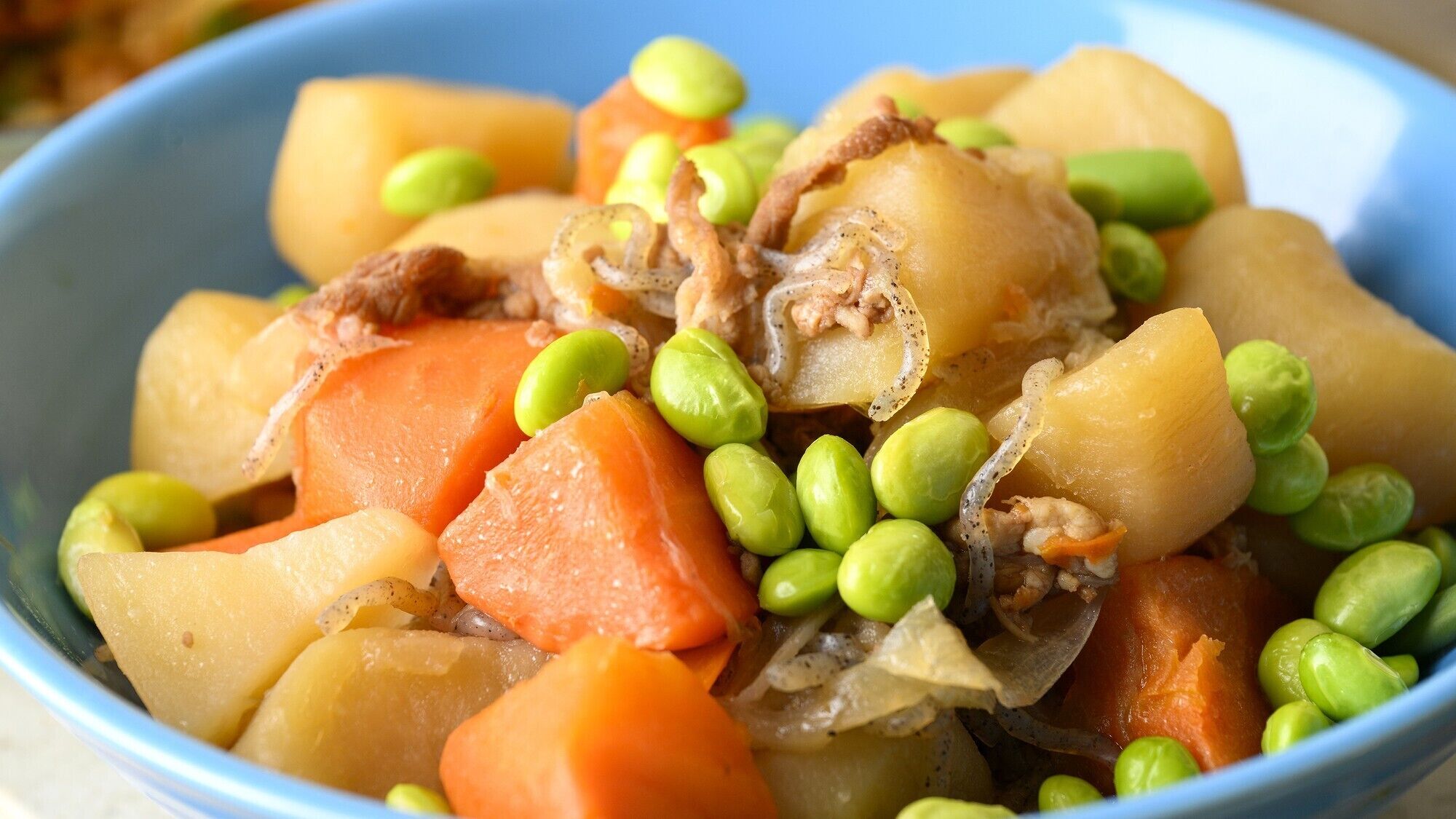 Uma tigela de comida com batatas, cenouras, ervilhas e carne.
